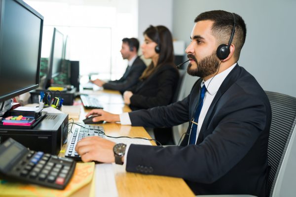 Sales representative talking with a customer Attractive latin executive offering customer service with a headset and offering tech support at a busy call center
