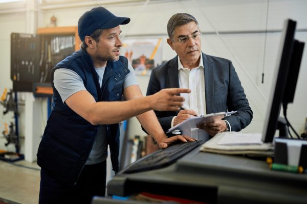 Auto repairman and manager cooperating while using computer in a Mid adult manager and car mechanic talking while using computer in auto repair shop.